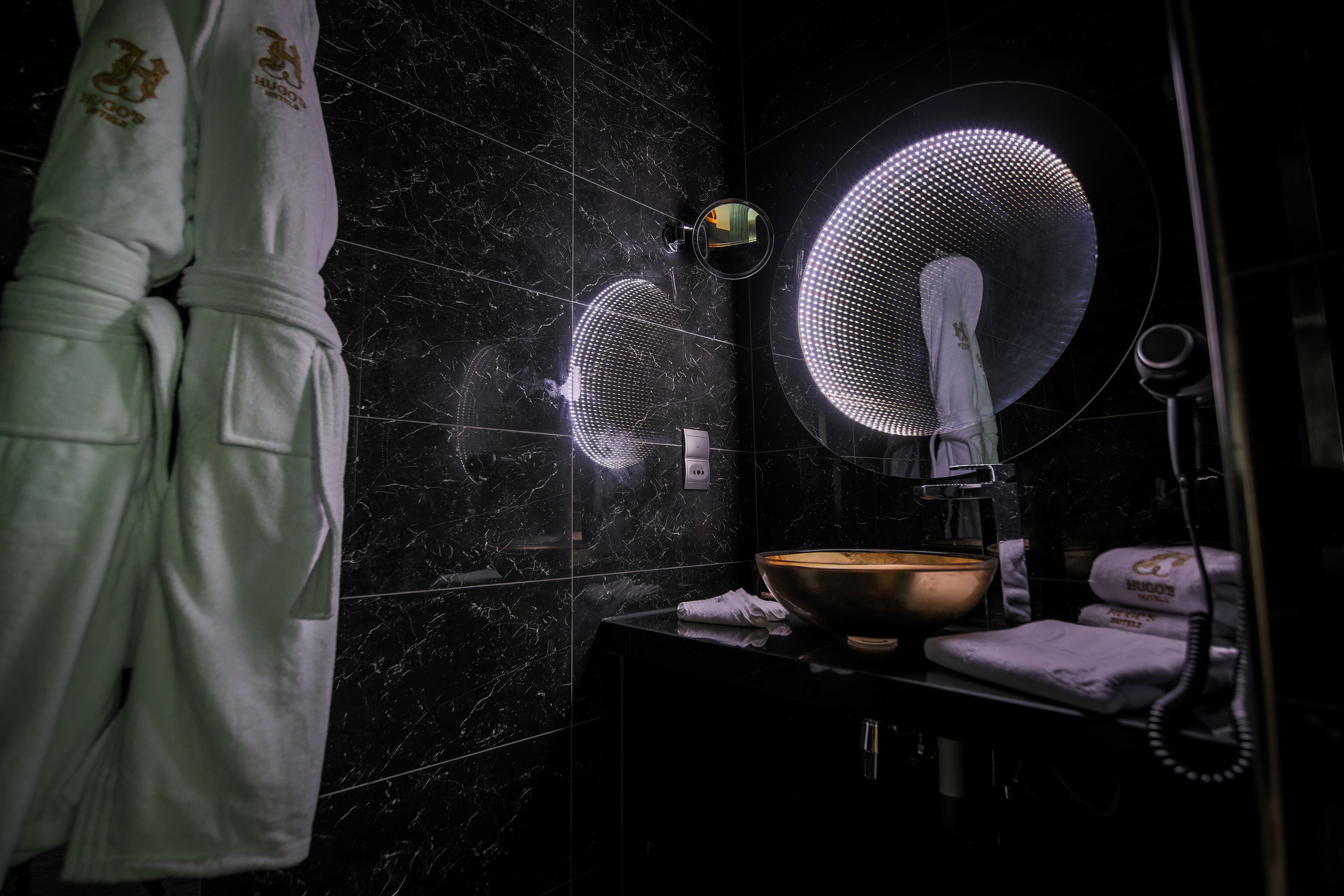 A bathroom with a black marble wall, a round mirror, a towel rack, and a sink with a bowl.