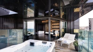 A modern rooftop lounge with a hot tub, seating area, and a view of the cityscape. - H Hotel (St. Julian's)