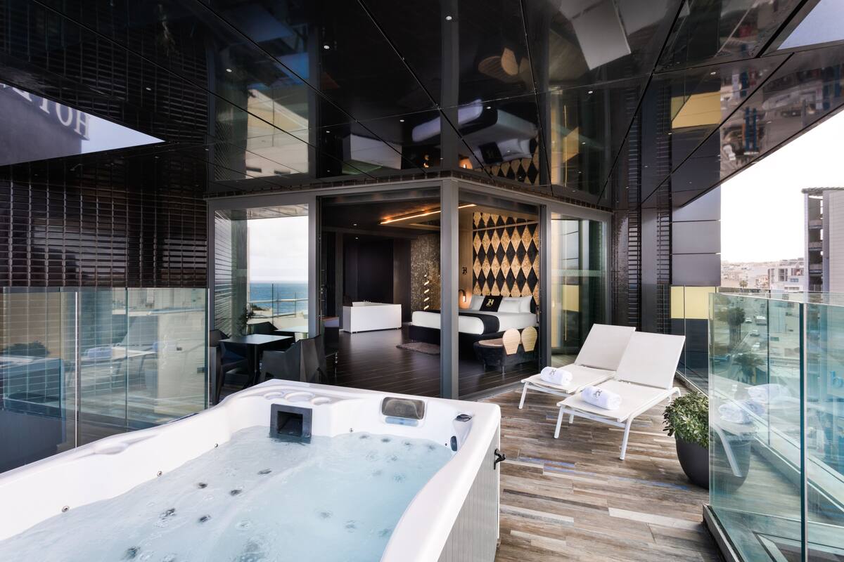 Un moderno salón en la azotea con jacuzzi, zona de estar y un espacio acristalado con un muro decorativo.