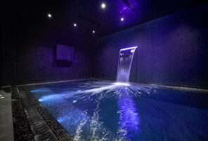 Una amplia piscina interior con una cascada y una pared oscura y con textura.