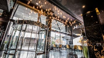 Un vestíbulo de hotel moderno con fachada de vidrio, un mostrador de recepción de mármol y una zona de estar con sillas.