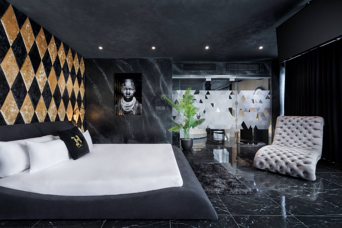 Un dormitorio moderno con una cama grande, un sillón capitonado y un muro con estampado geométrico.