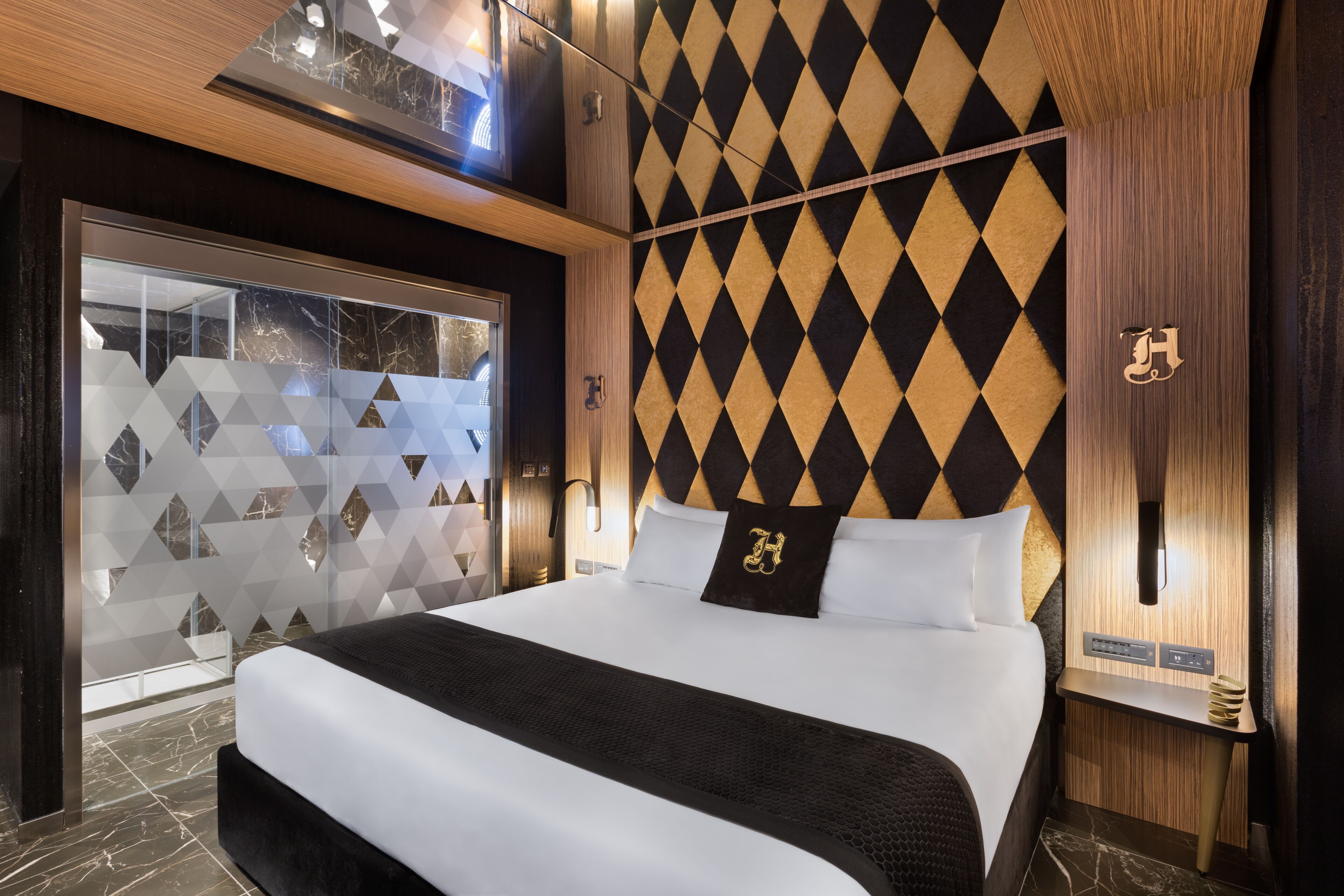 A modern hotel room with a large bed, a geometric-patterned wall, and a wooden ceiling.