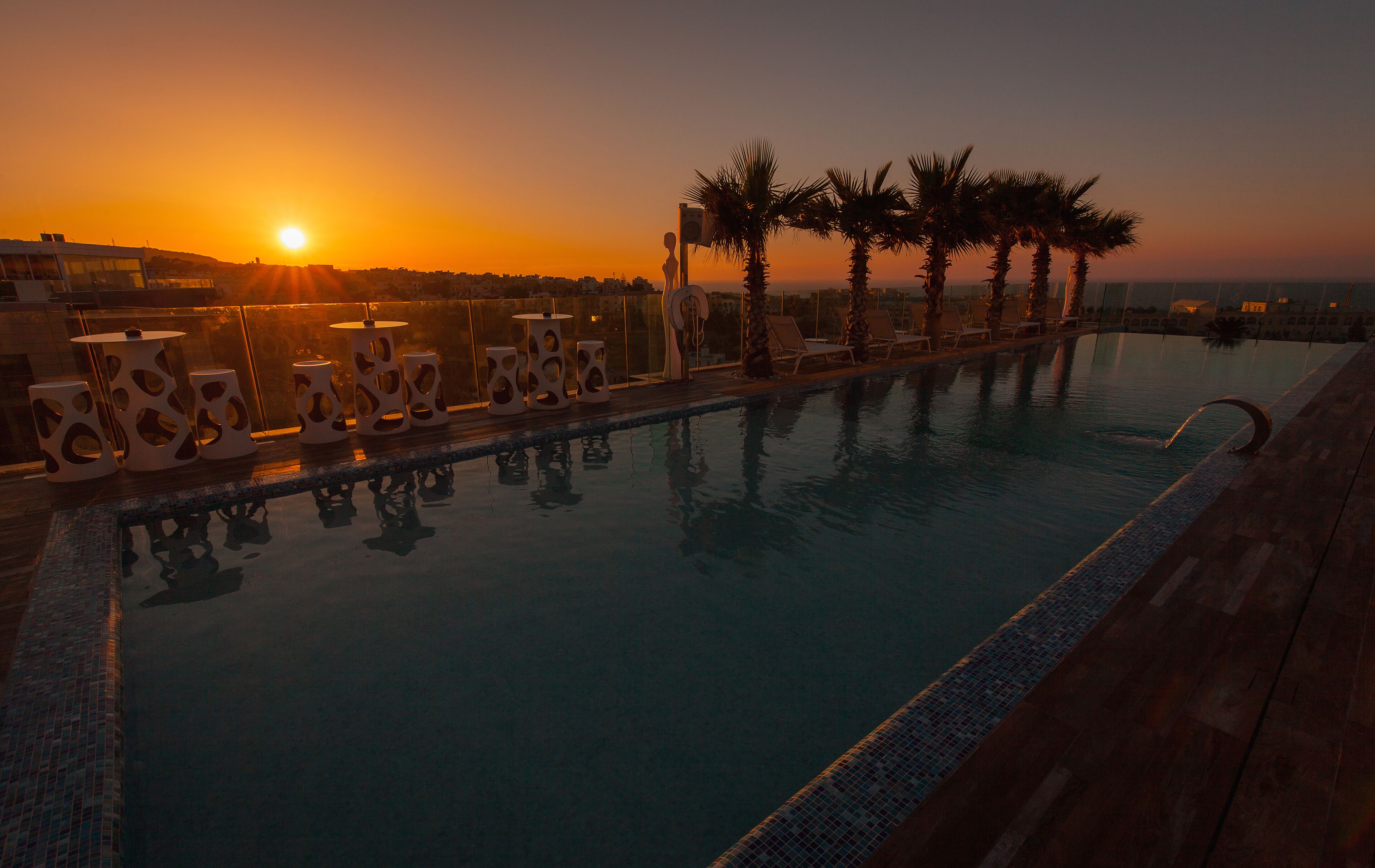 Una piscina con sillas de descanso y palmeras al atardecer.
