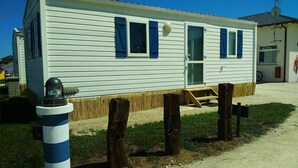 Una casa móvil blanca con contraventanas azules, un pequeño porche y una antena parabólica.