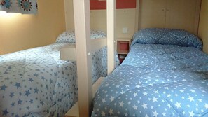 A room with bunk beds, each with a star-patterned bedspread. There is a small wooden shelf unit between the beds.