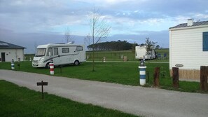 A caravan park with a white caravan, a small building, and a grassy field.