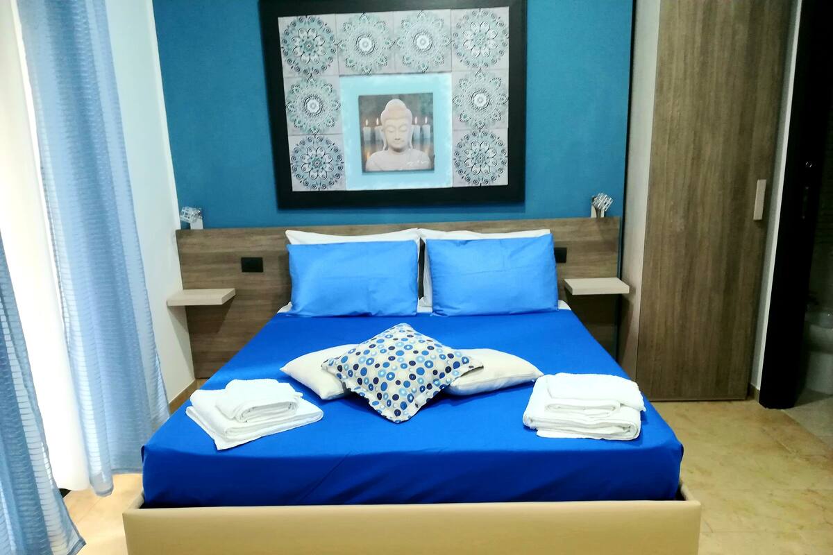 A neatly made bed with blue bedding, two pillows, and folded towels.