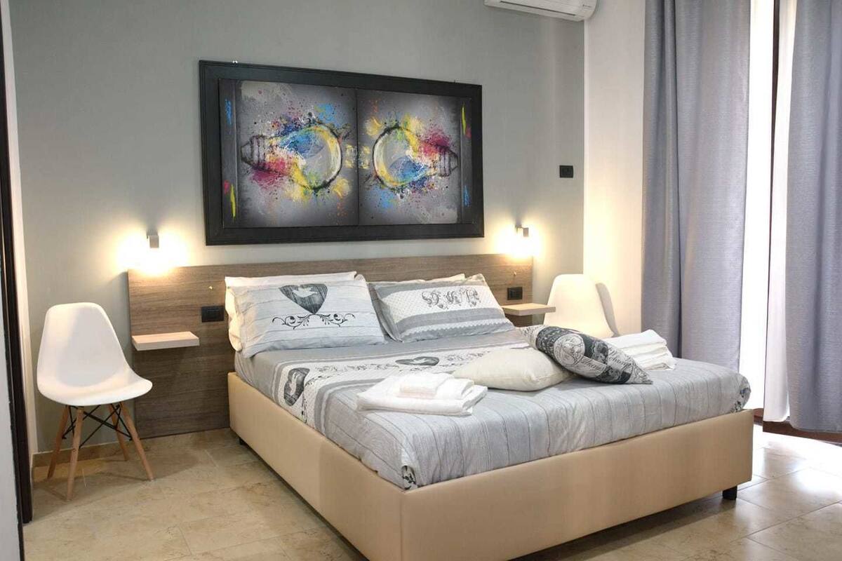 A modern bedroom with a large bed, two bedside tables, a headboard, and a large abstract painting above the bed.