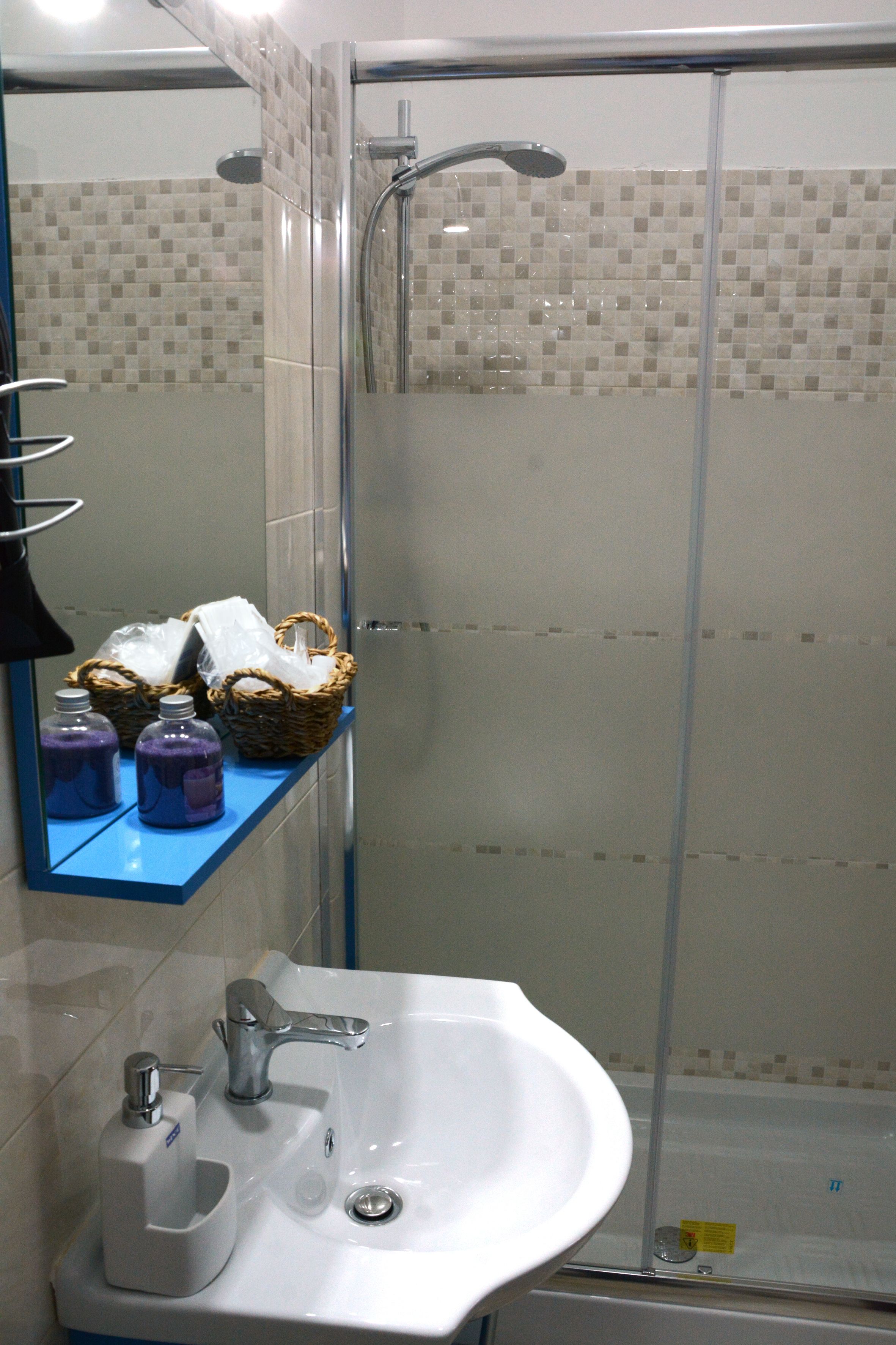 Une salle de bain avec une douche à parois de verre, un lavabo blanc doté d’un distributeur de savon et un miroir au-dessus du lavabo.