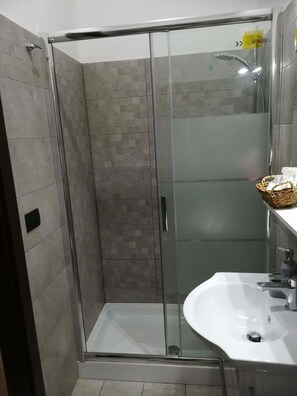 Un baño moderno con ducha envuelta en vidrio, un lavamanos blanco y pared con azulejos.