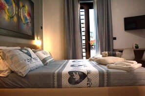 Una cama bien hecha con una colcha estampada, almohadas y una toalla doblada. Un televisor de pantalla plana está montado en la pared sobre la cama.