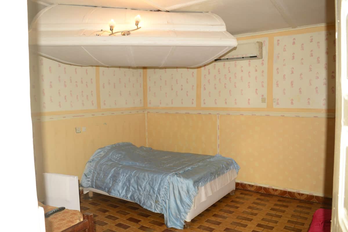 A small, single-bed room with a patterned wallpaper, a ceiling fan, and a radiator.