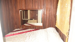 A room with a wooden paneled wall, a bed with a white and red bedspread, and a mirror reflecting the room.
