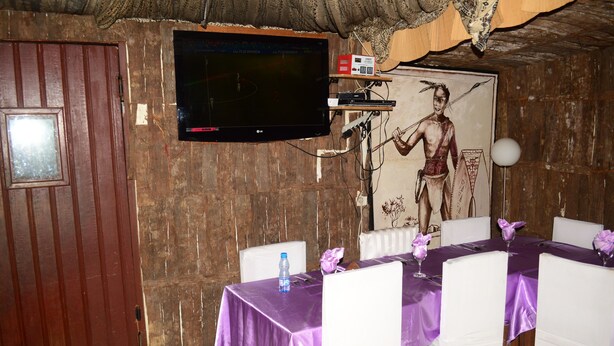 A dining area with a table set for four, a television mounted on the wall, and a mural of a warrior.