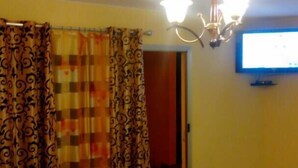 A room with a long table, a chandelier, curtains, and a television on the wall.