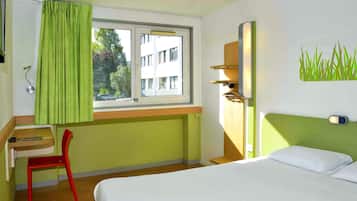 Een hotelkamer met een bed, een bureau, een stoel, een raam met gordijnen en een wandplank.