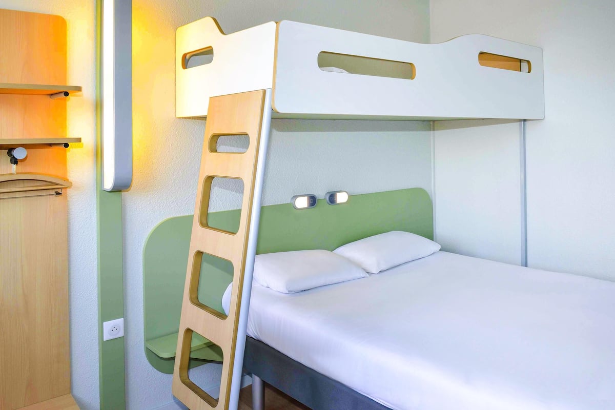 A bunk bed with a ladder, a bedside table, and a wall-mounted light fixture.