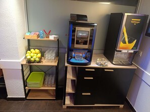 Una cafetera, una máquina expendedora y una presentación de frutas en un hotel.