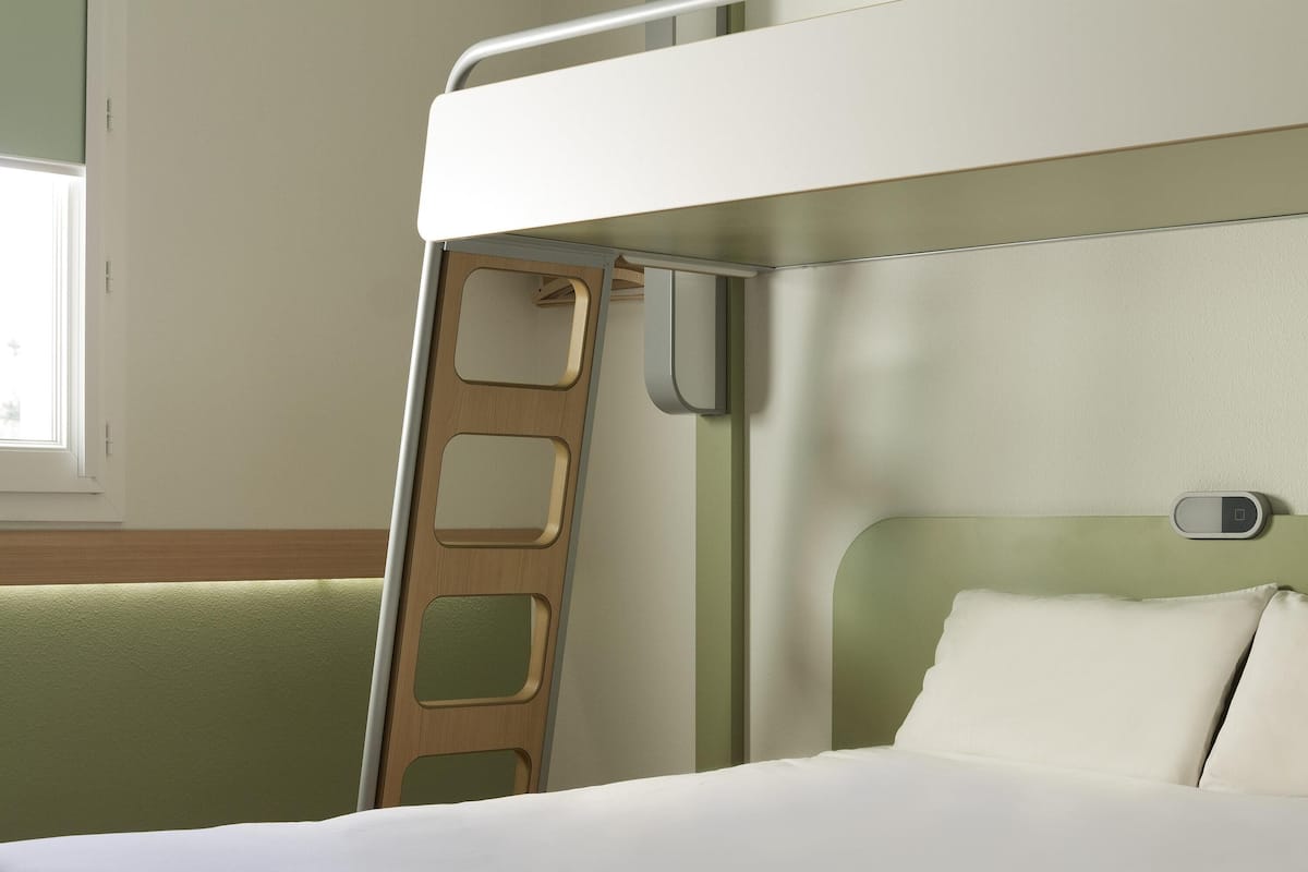Una cama litera con una escalera, una mesita de noche y una ventana.