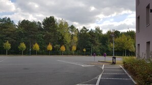 Ein Parkplatz mit markierten Stellplätzen, Bäumen und einem Gebäude im modernen Design.