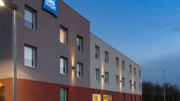 Ein modernes Hotelgebäude mit flacher Fassade, zahlreichen Fenstern und einem Schild mit der Aufschrift "ibis budget".