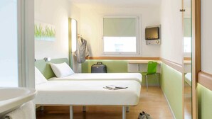 Ein Hotelzimmer mit Bett, Schreibtisch, Stuhl, Fernseher und Koffer.