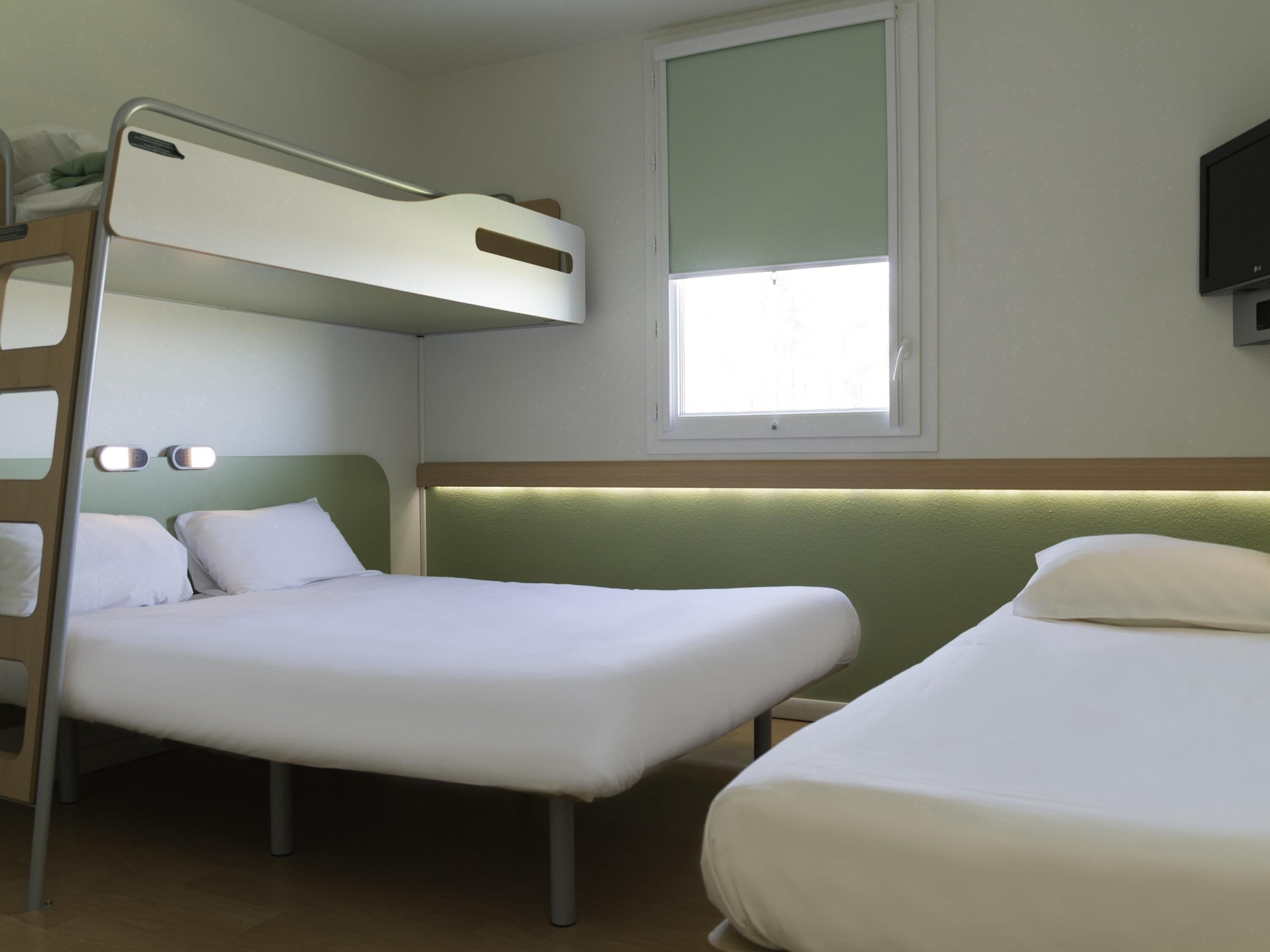 Habitación con literas, una cama plana y un televisor en la pared.