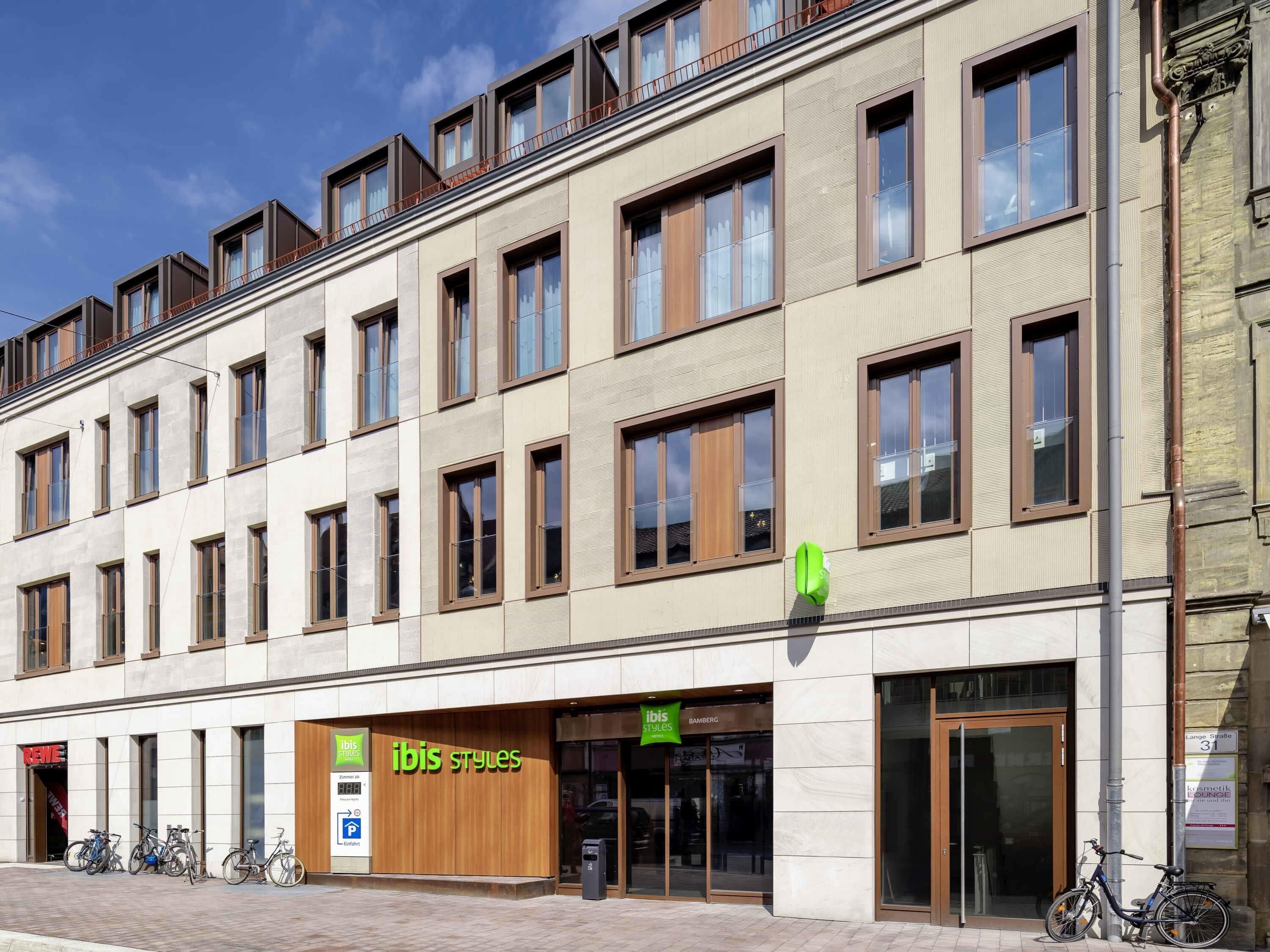 Um edifício moderno com várias janelas, uma fachada com a inscrição 'ibis styles' e bicicletas estacionadas na frente.