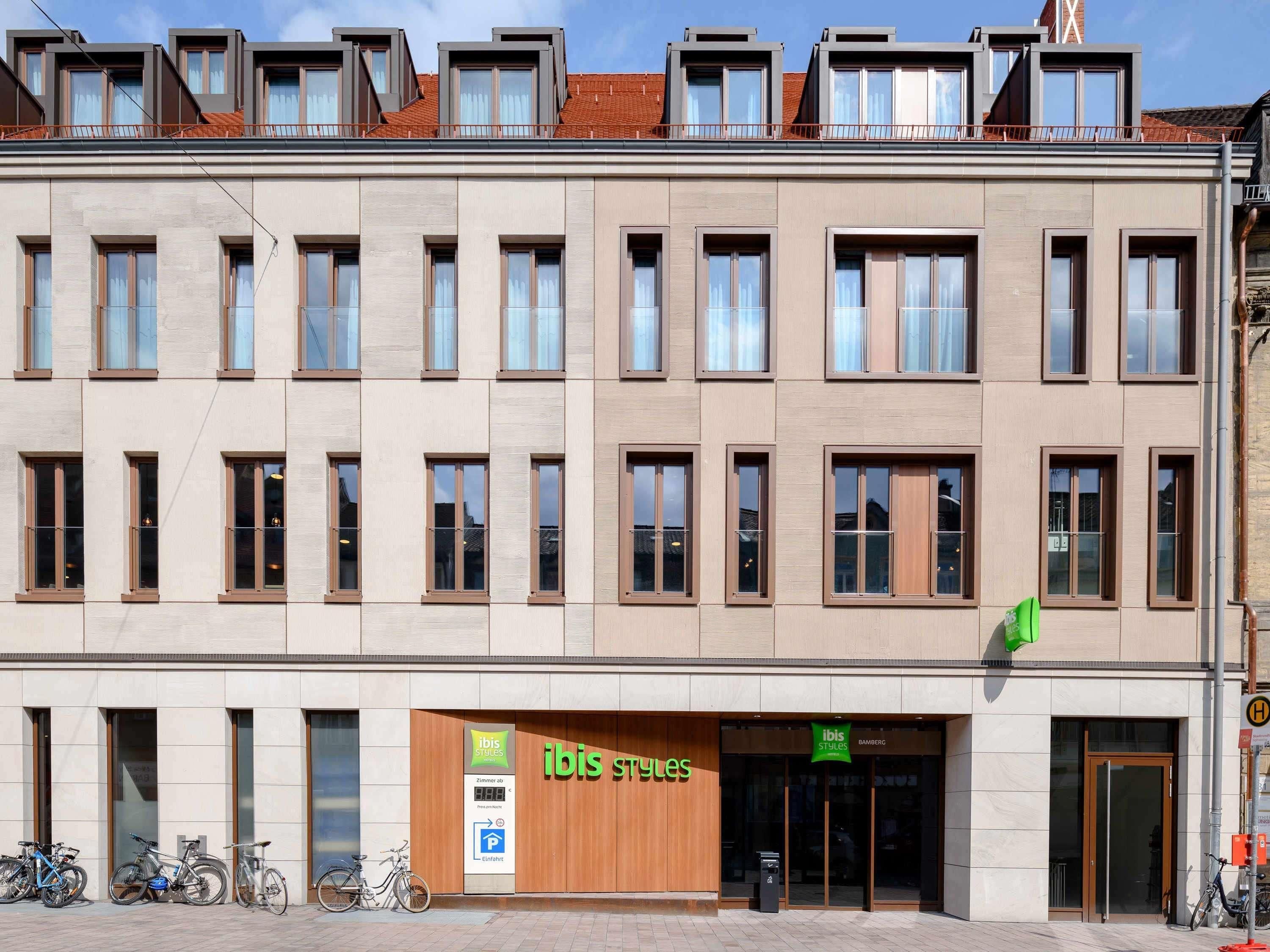 Ein mehrstöckiges Gebäude mit moderner Fassade, ein Laden mit einem grünen Schild und Fahrräder vor der Tür.