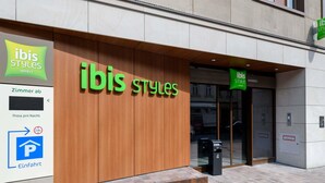 Entrada de un hotel con fachada de madera y un letrero que indica ibis Styles Hotels.