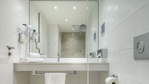 Un baño moderno con separador de vidrio, un lavamanos blanco, un espejo y un perchero para toallas.
