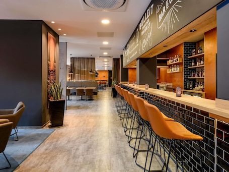 A bar area with a long counter, bar stools, and shelves with bottles.. Ibis Styles Bamberg Hotel