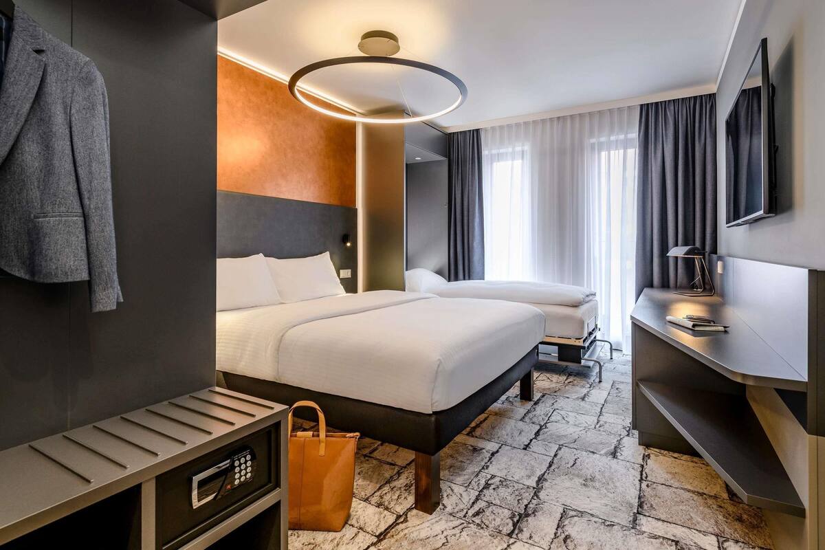 A modern hotel room with a large bed, a desk, a TV, and a bathroom.