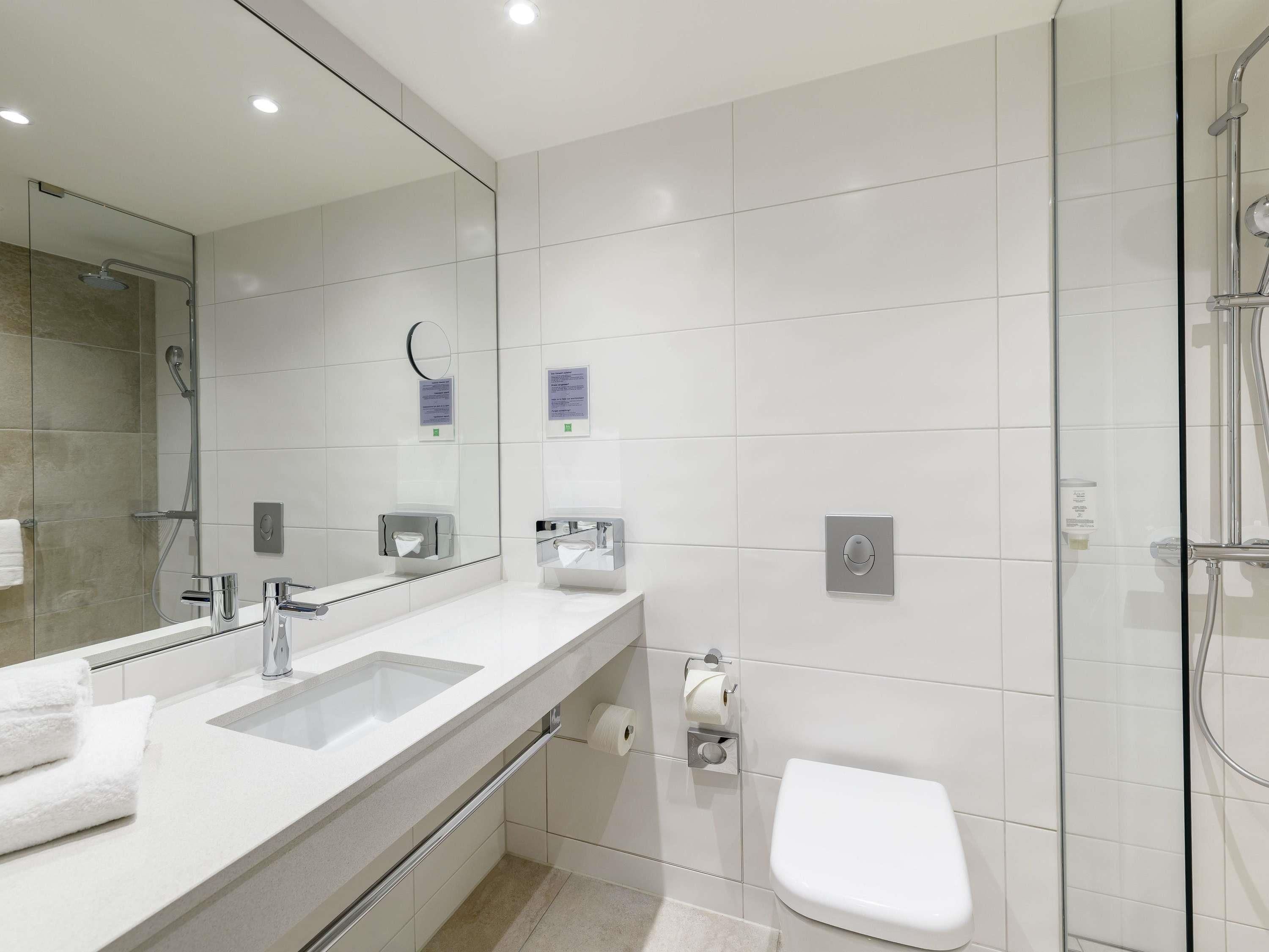 Ein modernes Badezimmer mit großem Spiegel, Waschbecken, Toilette und Duschbereich.