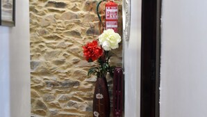 Un couloir avec un mur en pierre, un plancher en bois, un vase rempli de fleurs et un extincteur.