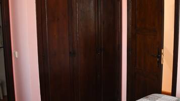 A bedroom with a large wardrobe, a bed with a floral bedspread, and a door leading to another room.