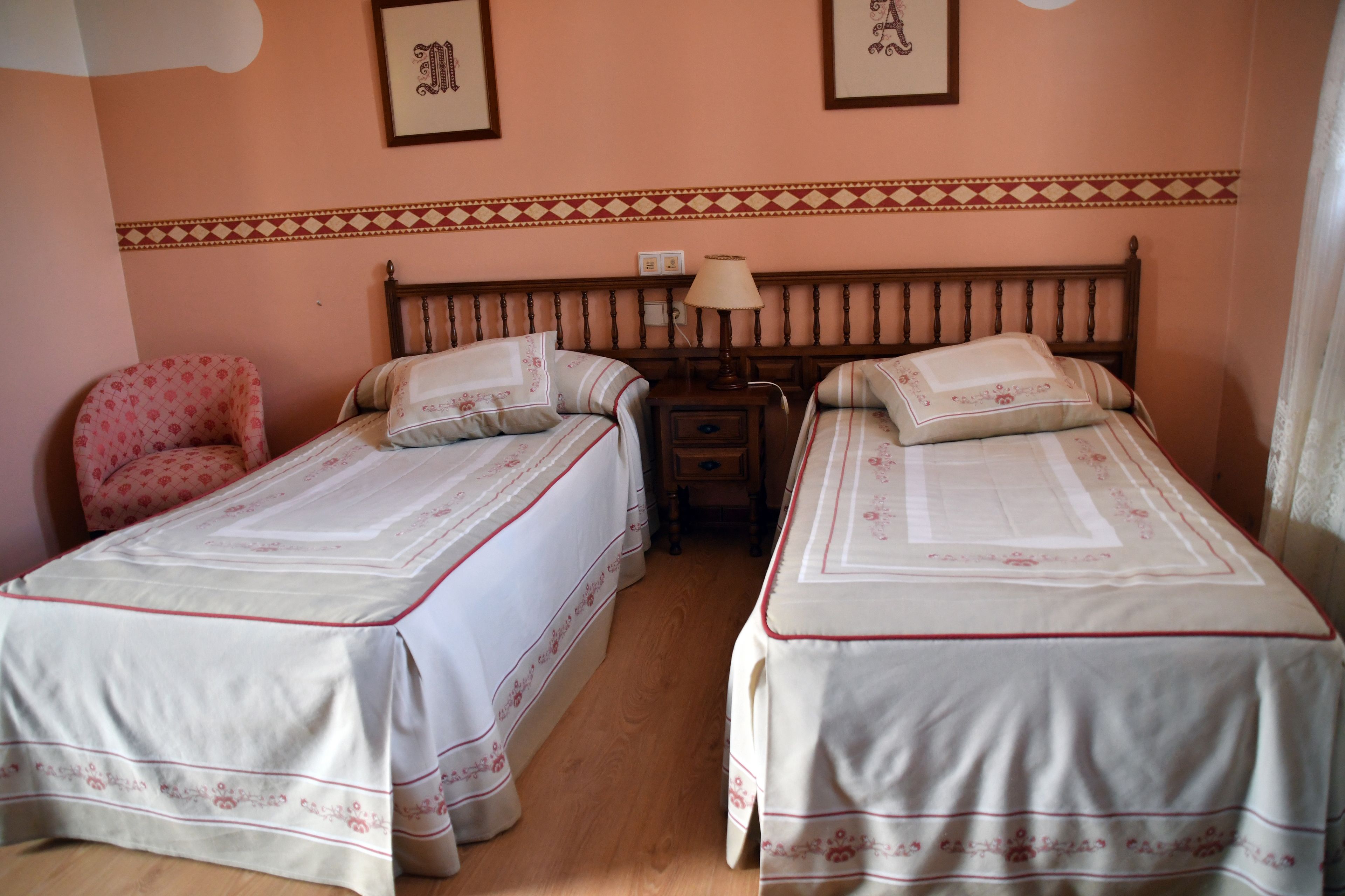 A room with two single beds, a wooden headboard, a small bedside table with a lamp, and a chair.