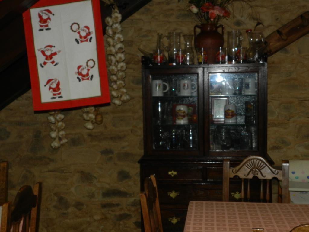 Un comedor con un aparador de madera que contiene cristalería y una mesa con mantel estampado.