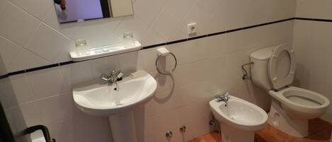 Un baño con un lavamanos, dos inodoros y un espejo.