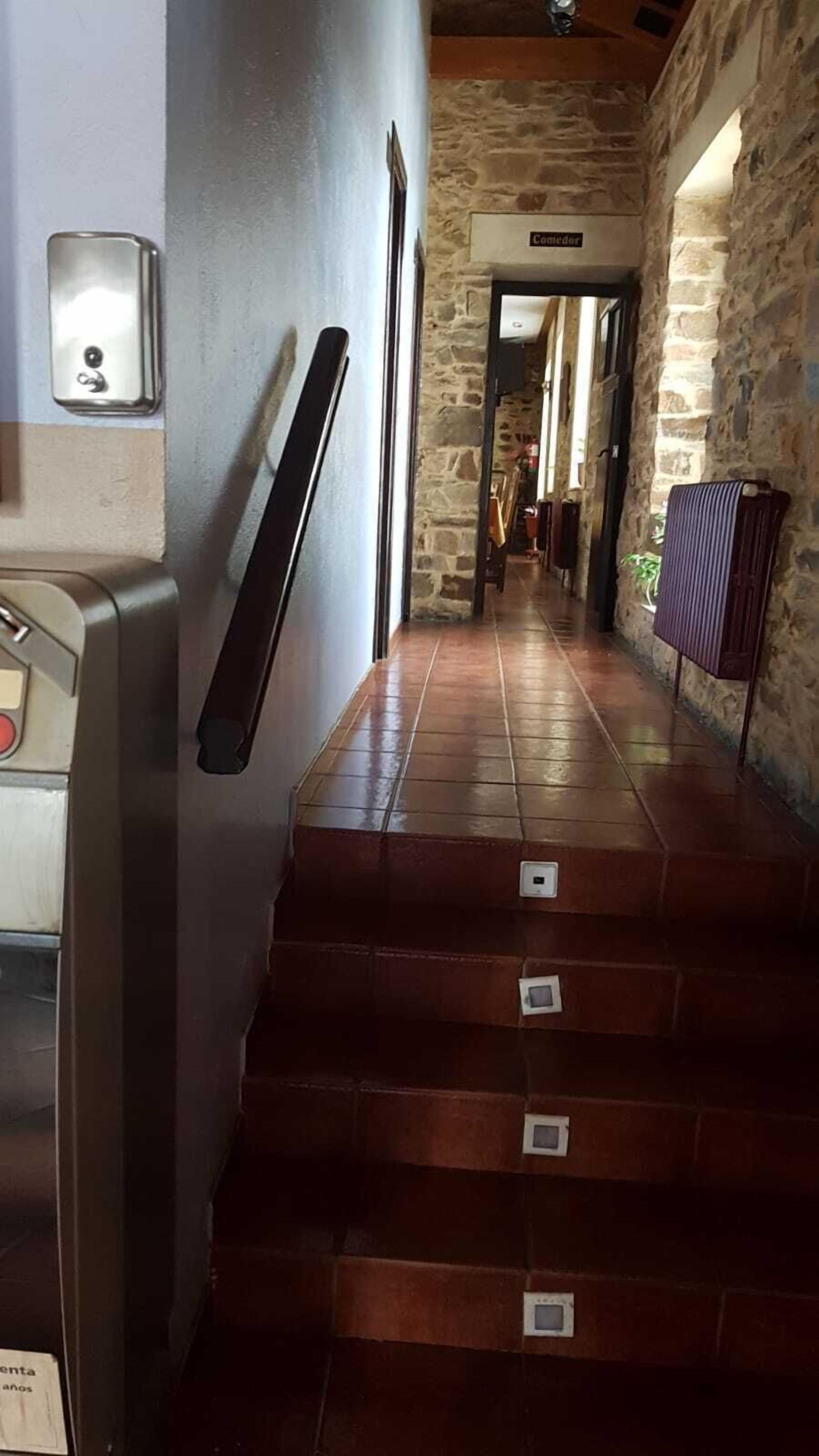Una escalera con barandilla, un muro de piedra y un cartel que dice 'Comedor'.