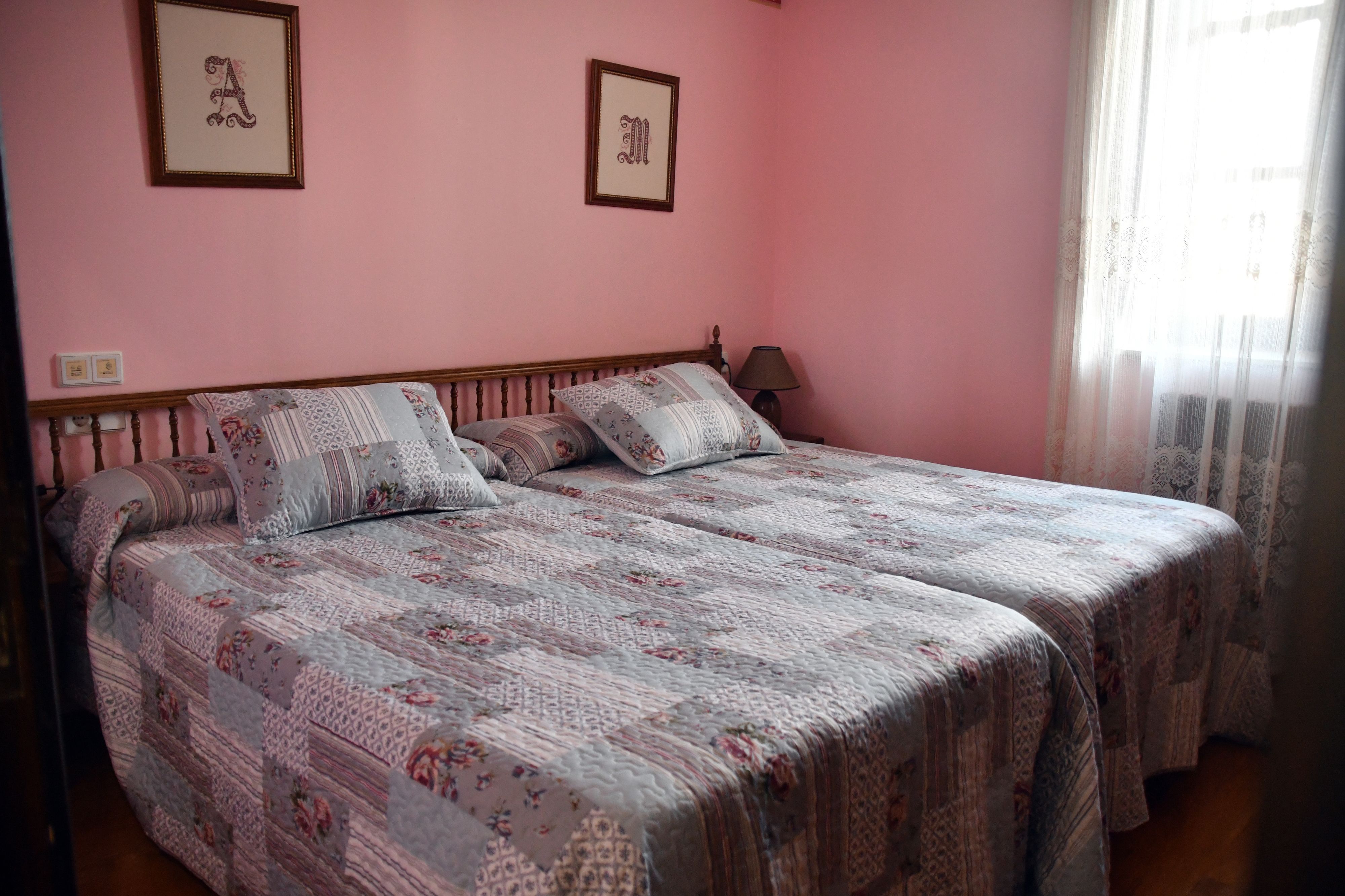 A double bed with floral-patterned bedding, a bedside table with a lamp, and two framed letters on the wall.