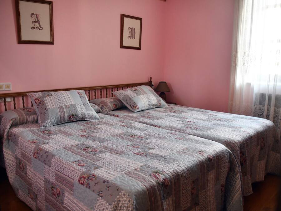 A double bed with floral-patterned bedding, a bedside table with a lamp, and two framed letters on the wall.
