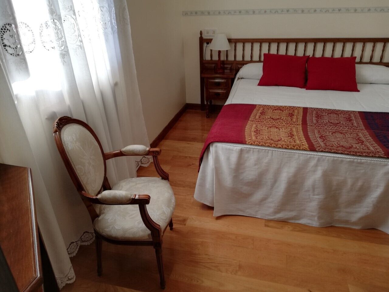 A bedroom with a wooden bed, a chair, a nightstand, and a window with curtains.