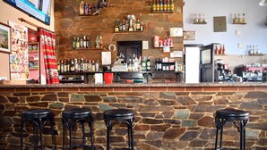 Un espace bar avec un mur en pierre, de nombreux tabourets, des étagères remplies de bouteilles et un appareil à café.