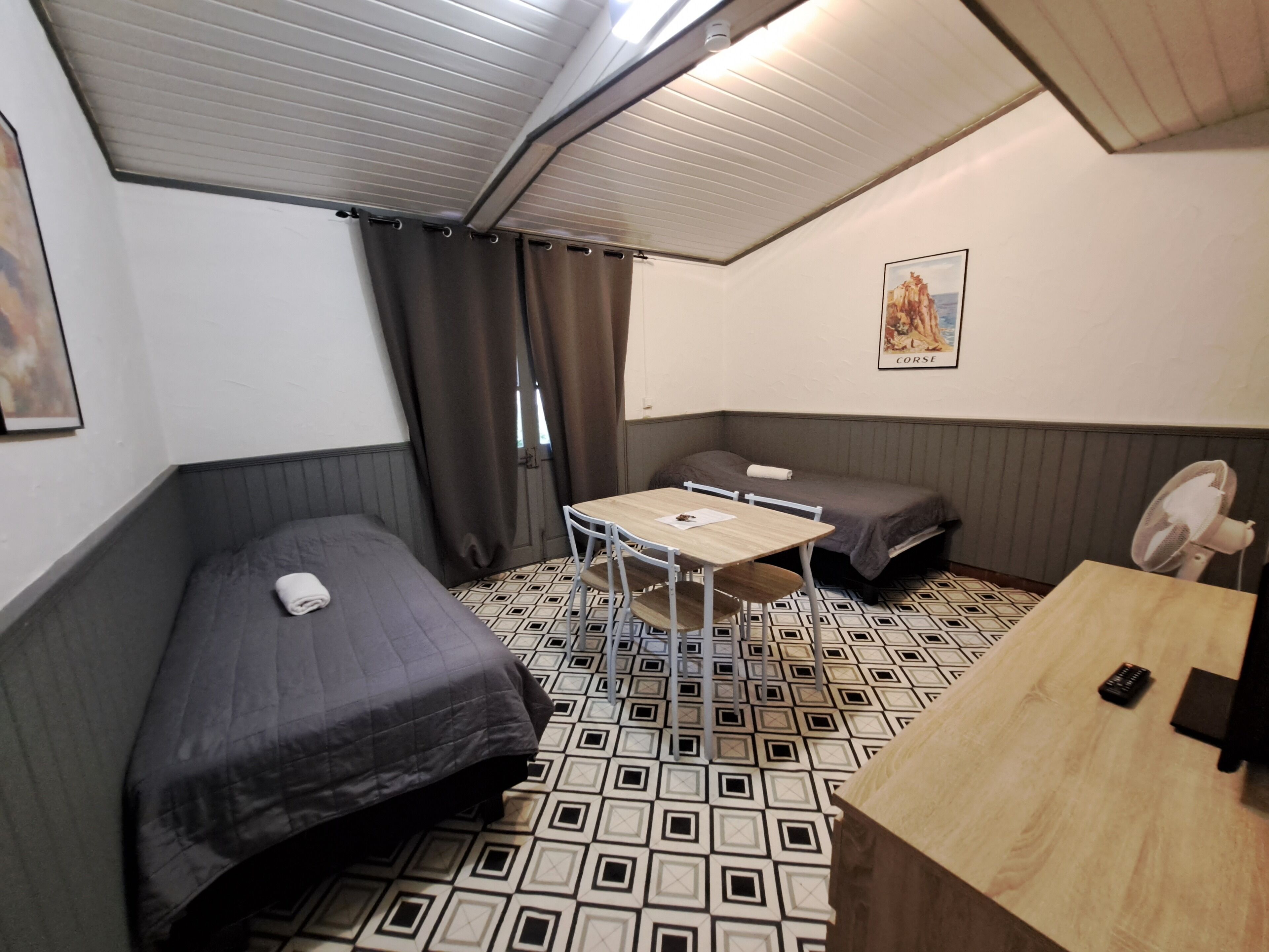 Une chambre de taille modeste, équipée de deux lits simples, d’une petite table et d’un ventilateur.