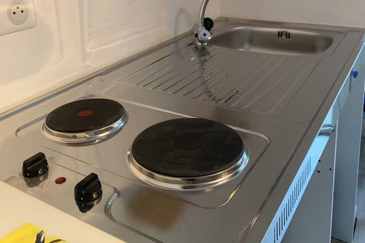 Une cuisine équipée d’une cuisinière en acier inoxydable, d’un évier et d’une étagère où sont rangés des verres.