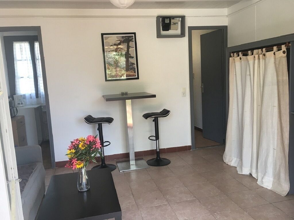 Una stanza con un tavolo nero, due sgabelli neri, un quadro appeso al muro, una tenda bianca e un vaso con fiori.