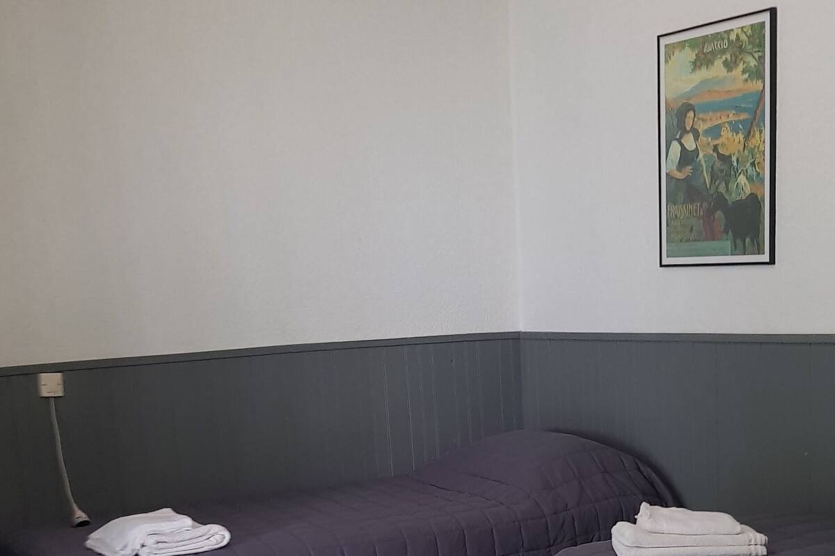 Une chambre avec deux lits, une table blanche et un tableau au mur.