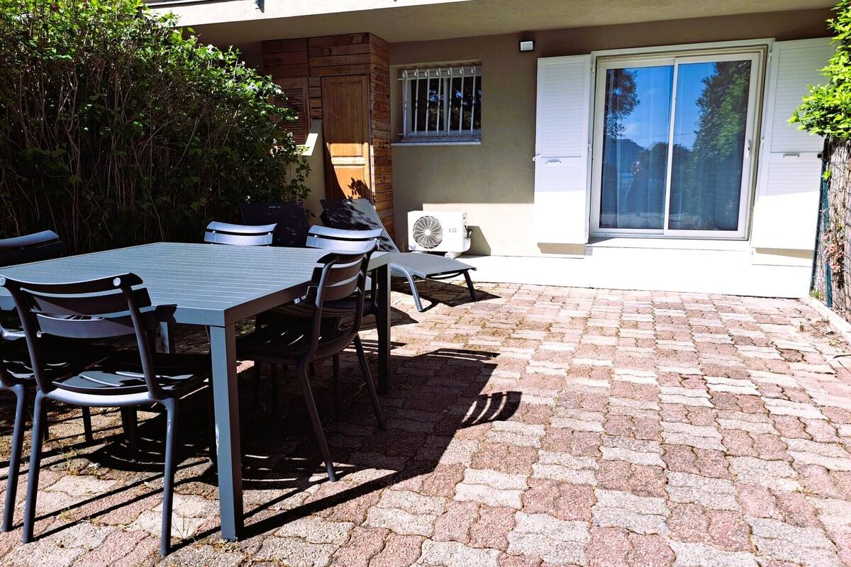Une terrasse avec une table et des chaises, un appareil de climatisation et une porte-fenêtre coulissante.